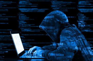 Hacker in a hooded jacket working on a laptop surrounded by digital code.