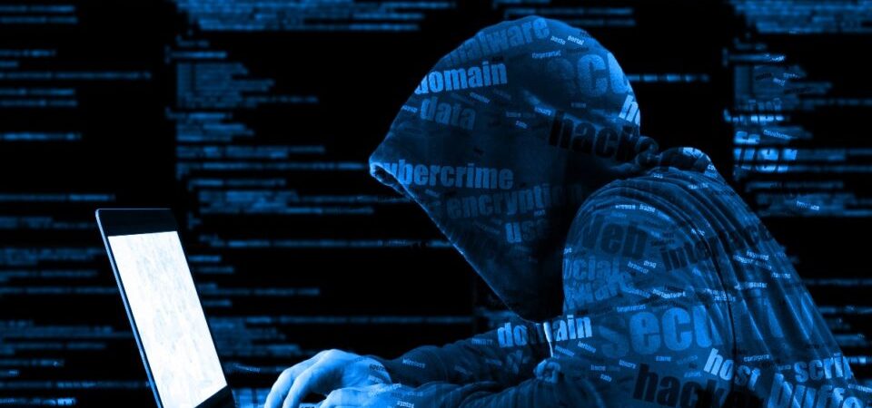Hacker in a hooded jacket working on a laptop surrounded by digital code.