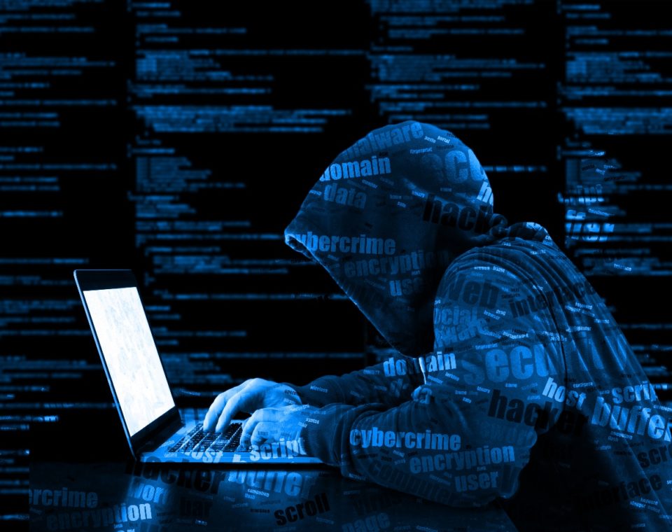 Hacker in a hooded jacket working on a laptop surrounded by digital code.